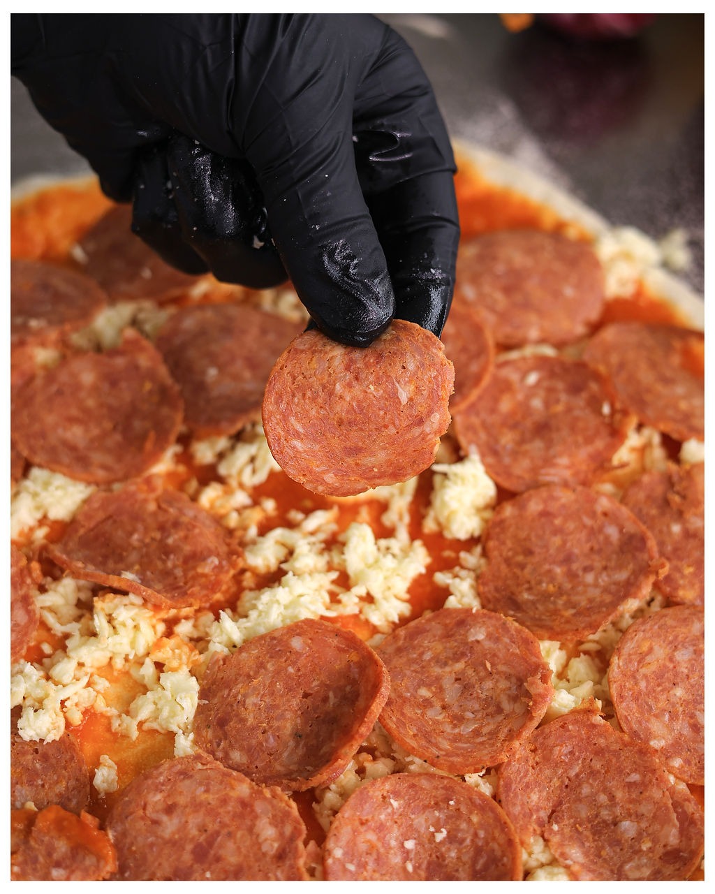 Pepperoni being placed on pizza